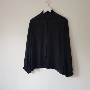 Svart långärmad skjorta med knappar strl S - Stilren svart skjorta med lång ärm och diskreta knappar framtill. Skjortan har en rak passform och är tillverkad i ett lätt, något transparent tyg som ger en luftig känsla. Perfekt för dig som gillar minimalistisk och clean stil.  Helt & fint skick 