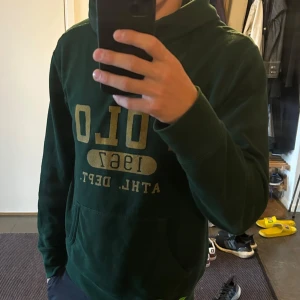 Polo ralph lauren hoodie - Säljer en sällsynt mörkgrön hoodie från polo ralph lauren i storlek M. Texten är skriven i gul/guldig text. Perfekt till hösten/vintern. Säljs då den inte används. 