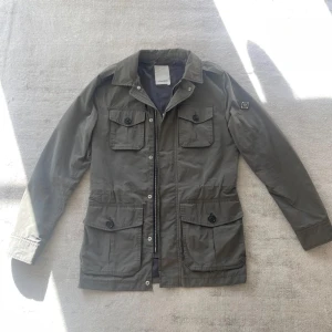J.Lindeberg Fieldjacket - Säljer en stilren olivgrön Field Jacket från J.Lindeberg i utmärkt skick! Storlek: XS men passar som Small. Endast använd ett fåtal gånger!
