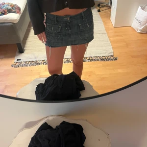 Jeanskjol med fransig kant och fickor - Säljer en blå jeanskjol med rå, fransig kant och fyra stora fickor med lock både fram och bak. Kjolen har bälteshällor, knapp och dragkedja framtill samt coola broderier på bakfickorna. Perfekt för dig som gillar en edgy och avslappnad stil.