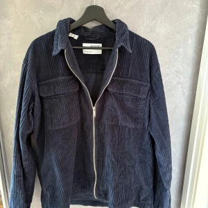 Mörkblå manchesterjacka från Selected - Snygg mörkblå overshirt från Selected i grov manchester. Jackan har dragkedja framtill, två stora bröstfickor med lock och klassisk krage. Perfekt för lager-på-lager och ger en cool, avslappnad vibe till din outfit.