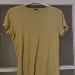 Gul basic t-shirt med kort ärm - Enkel gul t-shirt med rund halsringning och korta ärmar. Perfekt för en avslappnad stil och lätt att matcha med jeans eller shorts. T-shirten har en rak passform och är tillverkad i mjukt material.