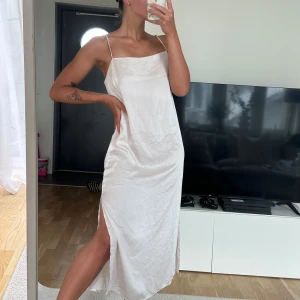 Ljus långklänning från H&M i satin - Supersnygg ljusbeige långklänning från H&M i satinliknande material. Klänningen har tunna axelband, rak halsringning och en slits på sidan som ger en chill vibe. Perfekt för sommarkvällar eller när du vill känna dig extra effortless.
