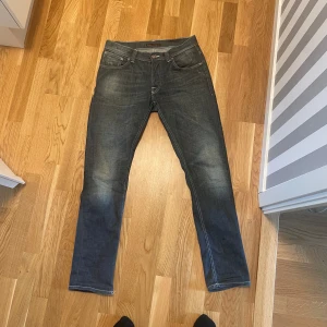Mörkblå jeans från Nudie Jeans - Säljer ett par mörkblå jeans från Nudie Jeans med snyggt slitna detaljer och klassiska bakfickor med vågformad söm. Jeansen har normal passform/slim och raka ben, tillverkade i mjuk bomull med en skön känsla. Perfekta för dig som gillar stilrena och tidlösa jeans. Säljer så mina ben blivit för stora och de sitter nästintill skinny på mig. Nästintill nyskick. W33 L32