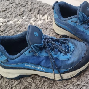 Blå sneakers från Merrell, strl 34 - Snygga blå sneakers från Merrell med robust sula och coola detaljer. Skorna har snörning och är gjorda i textil och syntetmaterial. Perfekta för dig som gillar en sportig och bekväm stil. Märket syns tydligt på sidan och sulan.