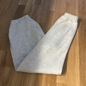 Ljusgrå mjukisbyxor med resår - Säljer ett par ljusgrå mjukisbyxor med resår i midjan och vid bensluten. Perfekta för chill dagar eller när du vill vara extra bekväm. Mjukt material och enkel stil som funkar till det mesta.