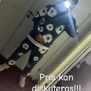 Denim tears, blå hoodie - Säljer en blå hoodie från Market med stora vita blommönster över hela tröjan. Hoodien har huva, magficka och långa ärmar. Perfekt för dig som gillar streetwear och vill sticka ut med en färgglad och unik stil.