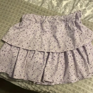 Ljuslila blommig volangkjol  - Supersöt ljuslila kortkjol från Name It med små blommor i lila, vitt och gult. Kjolen har volanger och resår i midjan för en bekväm passform🙌🏼 storlek 134/140 men passar även 146/152💕