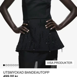 Svart utsmyckad bandeautopp - Snygg svart bandeautopp med utsvängd peplum och glittriga paljettdetaljer som ger en lyxig känsla. Toppen är axelbandslös och har en stilren, elegant look som sticker ut. Perfekt för dig som vill ha något extra till festen. Aldrig använd.