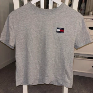 Grå t-shirt från Tommy Jeans XS - Snygg grå t-shirt från Tommy Jeans i storlek XS. Klassisk modell med rund hals och korta ärmar. Liten broderad logga på bröstet i rött, vitt och blått. Tillverkad i mjuk bomullsblandning för en skön känsla.