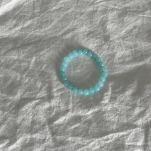 Blått pärlarmband med glans - Ett stilrent armband med runda, glansiga pärlor i ljusblått. Perfekt för dig som gillar en enkel men snygg accessoar som sticker ut lite extra. Elastiskt band gör det lätt att ta på och av. Passar till alla outfits och ger en fräsch vibe.