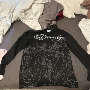 Svart långärmad t-shirt från Ed Hardy - Svart långärmad t-shirt från Ed Hardy med vit broderad logga och coolt linjemönster över hela framsidan. Köpt i julas helt ny och aldrig använd, lappen finns tom kvar på. Storlek small men väldigt oversized 