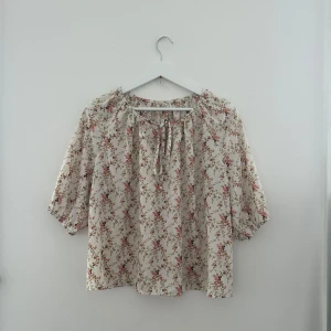 Blommig blus med knyt  - Supersöt blommig blus i ljusbeige med små rosa och gröna blommor. Ej använt! 