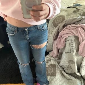 Blå bootcut jeans med slitna hål - Säljer ett par blå bootcut jeans med stora slitna hål över knäna och fransiga benslut. Fråga mig om du hsr frågor!!🌸🌸🌸🌸