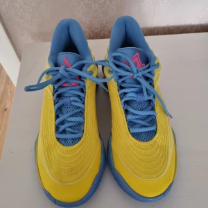 Nike sneakers i gult och blått - Basketskor Färgstarka Nike sneakers med vågig blå sula, gul ovandel och blå meshdetaljer. Swoosh-loggan är rosa och skorna har snörning. Perfekta för dig som vill sticka ut med en sportig och modern look. Materialet är syntet och mesh för bra andningsförmåga. Endast testad 1 gång nypris 1200 kr.