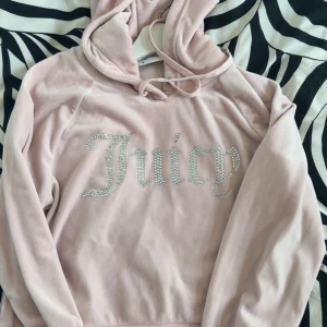 Juicy Couture cropped hoodie - Supermjuk ljusrosa hoodie från Juicy Couture i velour med glittrande Juicy-text i strass på bröstet. Klassisk huva med snörning och snygga metalldetaljer. Passar är även xs-s då det är min storlek egentligen. Perfekt för dig som älskar y2k och street. Säljer den pga den ej kommer till användning 