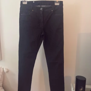Mörka denim skinny jeans med hög midja - Snygga mörka denimjeans med skinny fit och hög midja. Klassisk femficksmodell med silverfärgade nitar på bakfickorna. Materialet är stretchigt med 70% bomull, 28% polyester och 2% elastan för en bekväm passform.