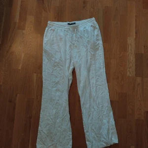 Vita linnebyxor med resårmidja - Luftiga vita linnebyxor med resår i midjan och raka, vida ben. Perfekta för varma dagar och enkel stil. Byxorna har snörning i midjan och sidfickor för en avslappnad look. Endast provade.