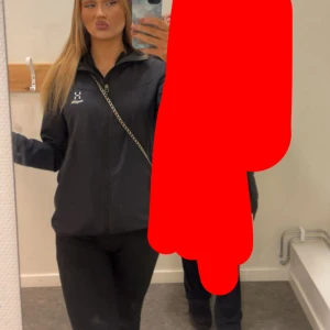 Svart vindjacka från Haglöfs - Säljer en svart vindjacka från Haglöfs med dragkedja framtill och hög krage. Jackan har en stilren design med diskret logga på bröstet och långa ärmar. Perfekt för dig som gillar en clean och sportig look.