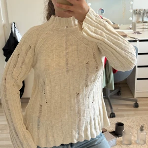 Ribbad stickad tröja  - Tröjan har hög hals, lång ärm och coola slitna detaljer längs hela plagget. 