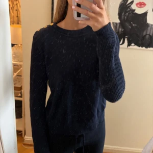 Mörkblå stickad tröja Ralph Lauren - Snygg mörkblå stickad tröja från Ralph Lauren med guldiga knappar på axeln. Klassisk rund halsringning och långa ärmar. Perfekt för dig som gillar stilrena detaljer och vill ha en tröja som sticker ut lite extra.