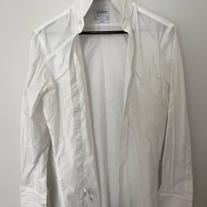 Vit slim fit skjorta från T.M. Lewin - Snygg vit skjorta från T.M. Lewin med slim fit-passning och klassisk krage. Skjortan är tillverkad i bomull och har långa ärmar med knappar vid manschetten. Non-iron material gör den enkel att hålla fräsch. Perfekt för dig som gillar stilrena och enkla plagg.