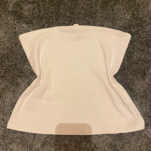Vit ribbad tubtopp i medium - Säljer en stilren vit ribbad tubtopp i storlek medium. Toppen är axelbandslös och har en bandeau-modell som sitter snyggt och bekvämt. Perfekt att matcha med jeans eller kjol för en clean look.