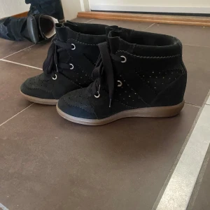 Svarta wedge sneakers Isabel Marant - Snygga svarta sneakers från Isabel Marant med kilklack och platt gummisula. Skorna är i mocka med dekorativa perforeringar och grova svarta snören. Perfekta för dig som vill ha en sportig men ändå trendig look.