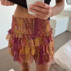 Färgglad volangkjol från Zara - Supersöt kort kjol från Zara med flera volanger och smock i midjan. Kjolen har ett paisleyinspirerat mönster i rött, gult och orange med inslag av rosa. lappen är bortklippt men skulle gissa på storlek S-m