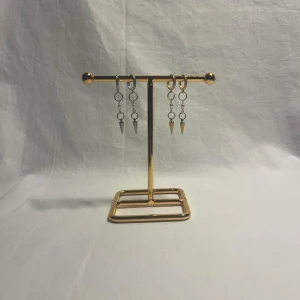 Örhängen med kedjor och konformade hängen - Säljer två par örhängen med coola kedjor och konformade hängen. Ena paret är i silverfärg och det andra i guld, båda med små ringar och detaljerade ytor. Perfekt för dig som gillar edgy och stilren vibe. Passar till att lyfta vilken outfit som helst.