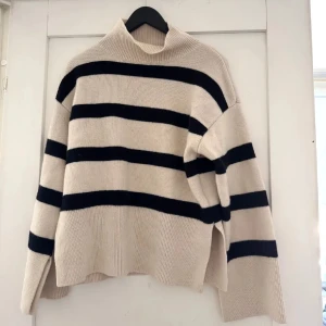 Randig polotröja i ullmix från H&M - Säljer en beige och svart polotröja från H&M i deras premium kollektion i ullblandning. Tröjan har breda svarta ränder och hög krage. Nypris 899kr
