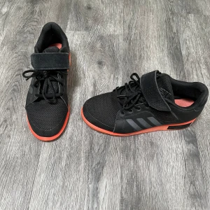 Träningsskor från Adidas  - Lyftarskor från Adidas. Skorna har snörning och en bred kardborre över vristen för extra support. Ovandelen är i mesh och syntet, vilket ger både andningsförmåga och stabilitet. Upphöjda i hälen. Perfekta för träning. Använda men bra omhändertagna. Nypris 1499. 