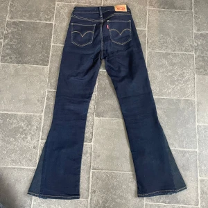 Levis jeans  - Säljer ett par mörkblå, midwaist Levi's jeans. Modellen har en rak passform från midjan till knät och utsvängda ben. Flare jeans i storlek w25. Klassiska och trendiga på samma gång! I fint skick.
