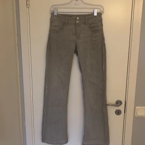 Low waist bootcut Gina jeans - Ljusgråa jeans med två silverknappar. Låg midja och bootcut-modell. Sthlmstil 