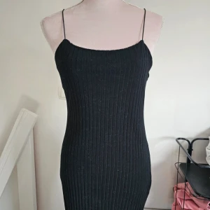 Svart ribbad långklänning från Zara - Svart långklänning från Zara med smala axelband och ribbad struktur. Klänningen är figurnära och har en enkel, stilren design som passar perfekt för dig som gillar minimalistisk stil. Materialet är mjukt och stretchigt för en bekväm passform.