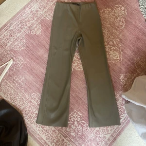 Utsvängda byxor i skinnimitation - Snygga kaki bootcut-byxor från Soaked in Luxuary, tillverkade i fusk skinnmaterial. Kick flare passform. Knappt använda. Dragkedja i sidan, elastiskt midjeband. Stretch. 