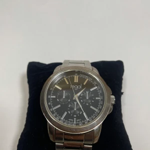 Regal silverfärgad klocka - Stilren klocka från Regal med svart urtavla. Okej skick syns i bilden mer bilder kan lösas. Bateri behöver bytas. Storlek syns, den kan även annpassas 