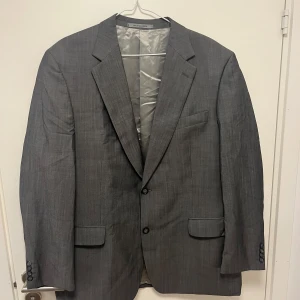 Grå kavaj från Oscar Jacobson - Snygg grå kavaj från Oscar Jacobson i klassisk modell med två knappar och fickor med lock. Tillverkad i 84% ull och 16% mohair, vilket ger en lyxig känsla och snygg struktur. Perfekt för dig som vill ha en stilren och tidlös look.