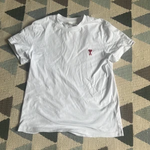 Vit t-shirt från Ami med rött hjärta - Vit t-shirt från Ami  med klassisk rund hals och korta ärmar. Passar runt 175-180 cm