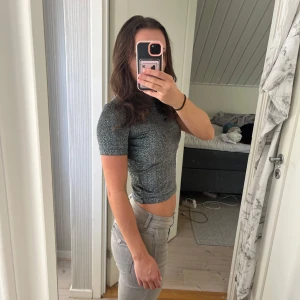 Silverglittrig festtopp från Stay - Säljer en glittrig croppad topp från Stay i svart och silver. T-shirten har korta ärmar och en tight passform som sitter snyggt mot kroppen. Perfekt till fest. 