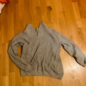 Grå ribbstickad half zip-tröja H&M - Mysig grå ribbstickad tröja från H&M med half zip-dragkedja i halsen. Tröjan har lång ärm och en relaxed fit, perfekt för lager på lager. Materialet är stickat och känns både mjukt och värmande. Enkel att matcha med jeans eller mjukisbyxor.