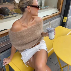 Beige offshoulder stickad tröja - Superfin beige stickad tröja med offshoulder-modell. Tröjan är fluffig och har en loose passform som ger en chill och trendig vibe. Perfekt att styla med kjol eller jeans för en snygg look. Materialet känns mjukt och skönt mot huden.