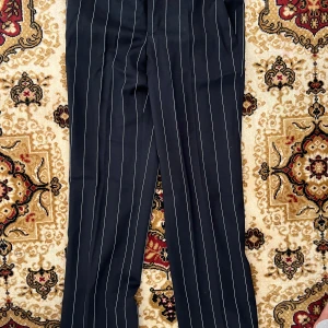 Svarta kostymbyxor från Zara Woman - Snygga svarta kostymbyxor från Zara Woman med vita vertikala ränder. Byxorna har klassisk rak passform, hysk- och hakstängning samt diskreta fickor. Perfekta för en stilren och trendig look.