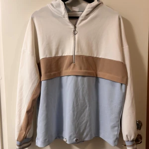 Hoodie i pastell med half zip och huva - Snygg hoodie i pastellfärger med breda block i vitt, beige och ljusblått. Tröjan har huva, lång ärm och en cool half zip-dragkedja framtill. Muddar med randiga detaljer vid ärmslut och avslappnad passform. Perfekt för en chill och trendig look. Perfekt för träning eller aktiviteter utomhus 
