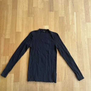 Svart ribbad långärmad tröja  - Svart ribbad långärmad tröja från Name It. Det är storlek 158/164 men passar xs-s. Tröjan har små volanger i kragen och ärmarna, samt längst ner på tröjan. Tröjan är aldrig använd.