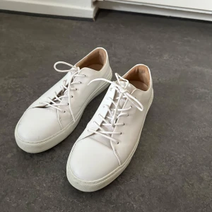 Vita sneakers i skinn från Tiger of Sweden - Snygga vita sneakers i stilren design med rund tå och platt sula. Skorna har klassisk snörning och är tillverkade i slätt skinn med ljus insida. Skorna är i mycket fint skick och är knappt använda. Nypris 2500kr.