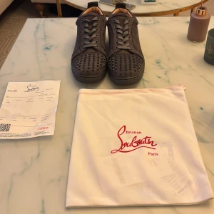  Gråa Christian Louboutin sneakers med nitar - Säljer ett par svarta sneakers från Christian Louboutin med coola svarta nitar på tån. Skorna har snörning och är tillverkade i mocka med platt sula och rund tå. Kommer med originalpåse och kvitto. 
