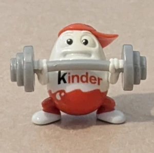Unik samlarfigur från Kinder som styrketränar - Bilderna visar en cool samlarfigur från Kinder, formad som ett ägg med röd keps som styrketränar Figuren är av plast och har en sportig, rolig stil som passar samlare eller träningsintresserade. 