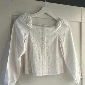 Vit blus med broderade blommor från ONLY. Barnstorlek - Oanvänd vit blus från Kids ONLY med broderade blommor och knappar framtill. Långärmad modell med puffiga axlar och smockad rygg.