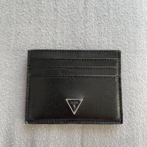 Svart korthållare från Guess i skinn - Slimmad svart korthållare från Guess i äkta skinn med stilren struktur. Har flera kortfack på båda sidor och en metallogo framtill. Perfekt för dig som vill ha koll på korten utan att ta plats i fickan.